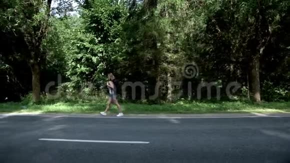 年轻女子背着背包在森林背景的道路上行走视频的预览图