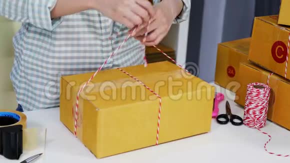 女企业家的手正在绑绳子把产品包装在包裹箱里准备送到家庭办公室的顾客手中视频的预览图