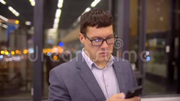 在城市的夜晚人们使用智能手机上的应用程序短信英俊的年轻商人用智能手机微笑快乐视频的预览图