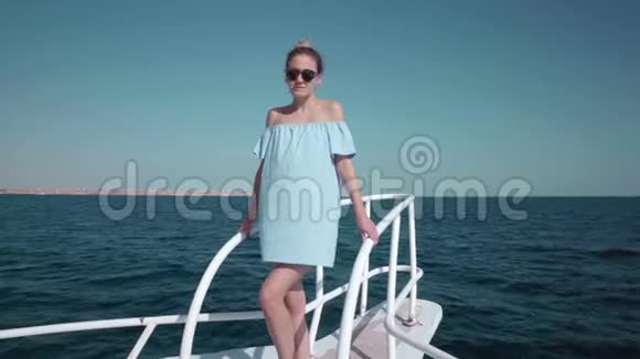 一个年轻漂亮的高加索女人在游艇上穿着蓝色连衣裙和太阳镜的肖像假期的概念视频的预览图