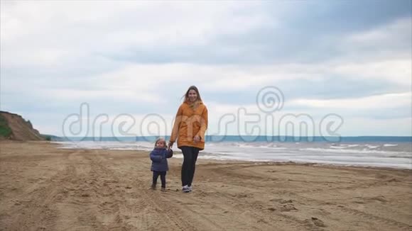 妈妈和她最近学会走路的小儿子一起沿着海滩散步视频的预览图
