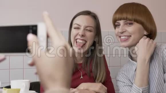 年轻美丽的白种人女孩正在智能手机上拍摄她的两个女朋友坐在咖啡馆里的照片女孩视频的预览图