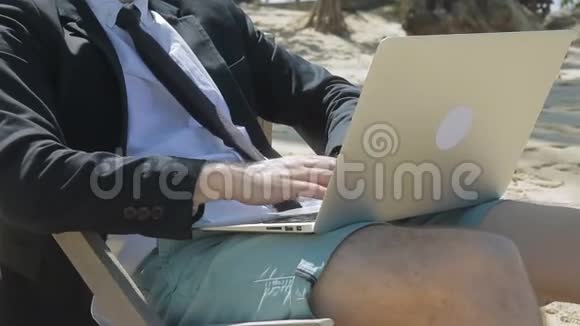 商人坐在海滩上膝盖上放着笔记本电脑视频的预览图