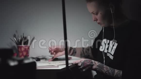 年轻的纹身艺术家朋克女子在灯光下在书桌前画画视频的预览图