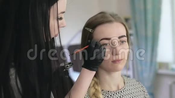 化妆师和模特长着大眼睛的年轻金发碧眼带着辫子化妆师给一个漂亮的女孩画眉毛视频的预览图