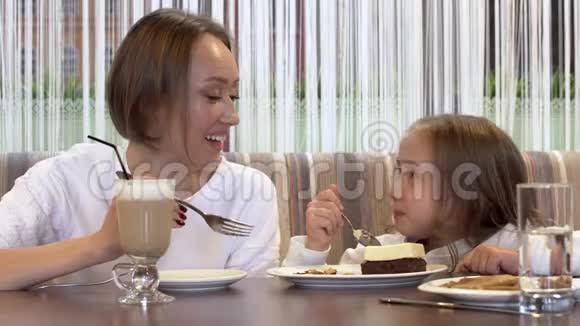 美丽的年轻母亲和小女儿一起在一间舒适的咖啡馆里吃蛋糕视频的预览图