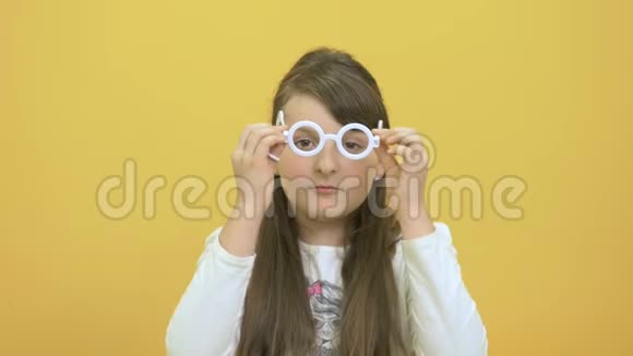 戴塑料眼镜的小女孩在黄色背景上展示塑料剪刀视频的预览图