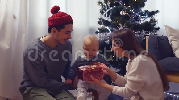 家中圣诞树附近有圣诞礼物的家庭和宝宝儿童打开礼品盒视频的预览图