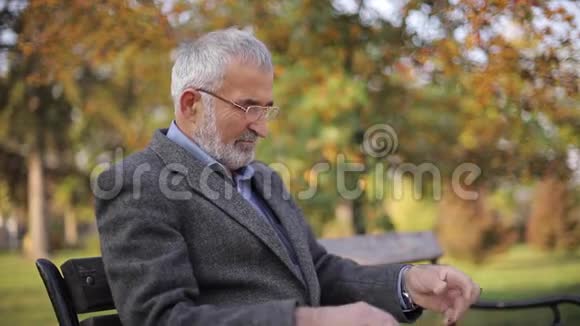 大胡子老人戴眼镜在秋天公园看报纸英俊的白发男子早早地坐在长凳上视频的预览图