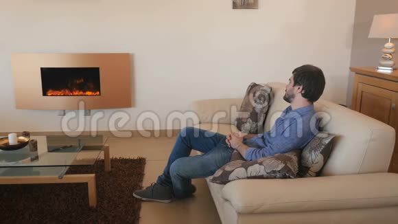 穿牛仔裤的帅哥在客厅的电壁炉附近放松视频的预览图