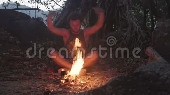 白种人野蛮人在黄昏的热带森林里燃烧小篝火用米饭煮水壶吃晚餐视频的预览图