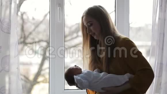 母亲站在窗边抱着新生的孩子视频的预览图