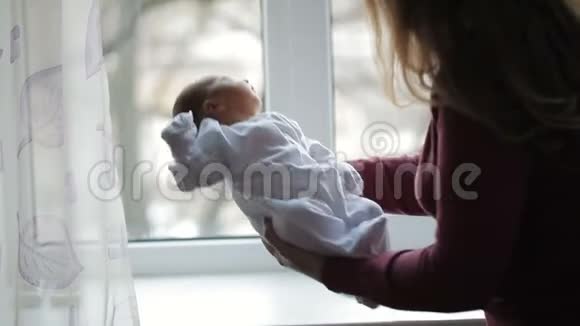 母亲站在窗边抱着新生的孩子视频的预览图