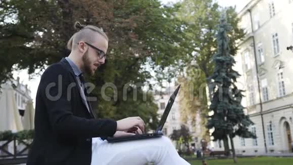 一个戴着眼镜留着胡子的人坐在露天的楼梯上在电脑上工作视频的预览图
