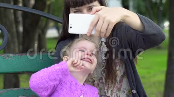 妈妈和可爱的小女儿在公园里用智能手机自拍视频的预览图