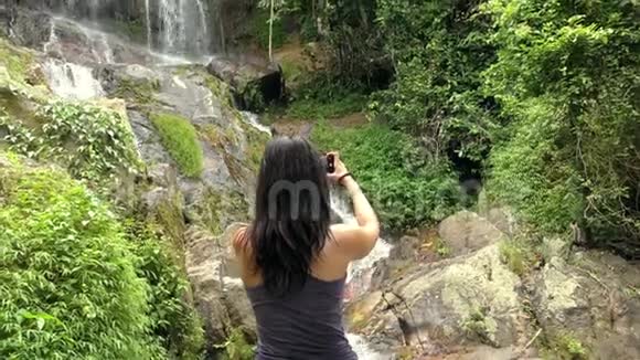 女孩在手机上拍一张瀑布的照片视频的预览图