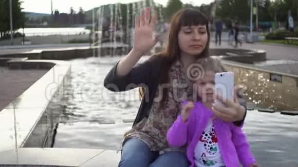 妈妈和可爱的小女儿在公园里用智能手机自拍视频的预览图