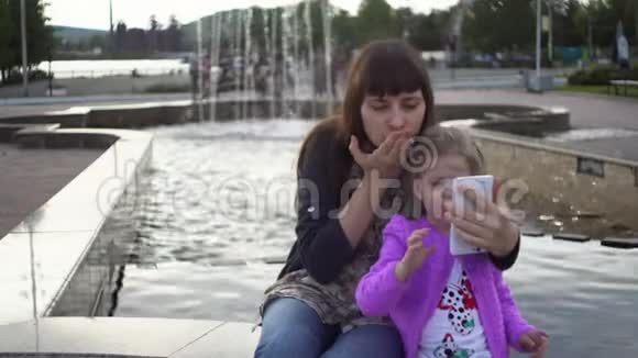 妈妈和可爱的小女儿在公园里用智能手机自拍视频的预览图