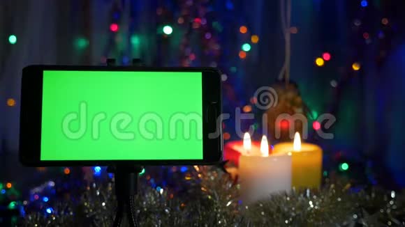绿色屏幕的智能手机在新年的背景下闪烁的花环燃烧的蜡烛视频的预览图