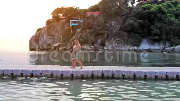 在美丽的日落中两个女朋友在热带岛屿的海上桥上散步1920x1080视频的预览图