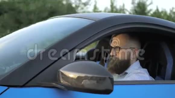 戴眼镜坐在方向盘后驾驶跑车的严肃的留胡子的年轻商人视频的预览图