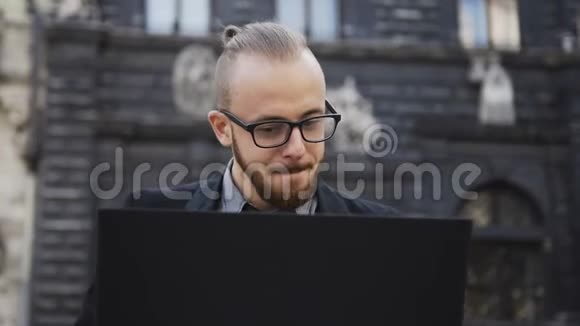 一个戴着胡子眼镜的英俊有前途的男人在露天电脑上工作视频的预览图