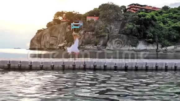在令人惊叹的日落中年轻快乐的女人在热带岛屿上的海桥上旋转1920x1080视频的预览图