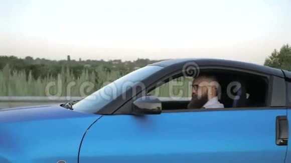 戴眼镜坐在方向盘后驾驶跑车的严肃的留胡子的年轻商人视频的预览图