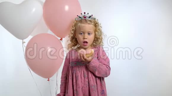 可爱的小女孩带着气球在她的生日吃甜甜圈被隔离在白色的背景上视频的预览图