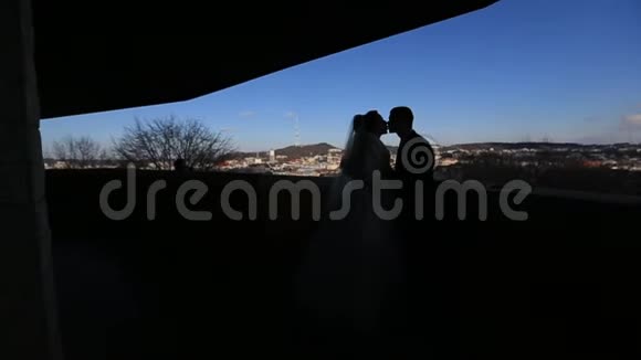 在阳台上和城市景观一起温柔地亲吻着新婚夫妇的剪影视频的预览图