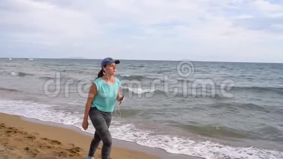 运动的女人带着耳机沿着海滩散步慢动作视频的预览图