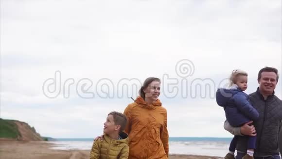 一个幸福的家庭孩子们穿着温暖的衣服在一个刮风的日子里在海边漫步视频的预览图