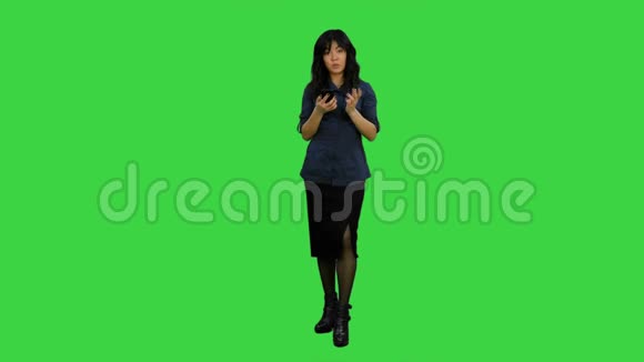 年轻的亚洲女性站在智能手机上与绿色屏幕上的摄像机交谈Chroma键视频的预览图