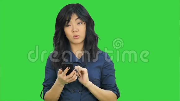 亚洲女商人在智能手机上阅读演示文稿看绿色屏幕上的相机Chroma键视频的预览图