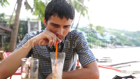 英俊的年轻人坐在海边的海滩咖啡馆里喝鸡尾酒慢动作3840x2160视频的预览图