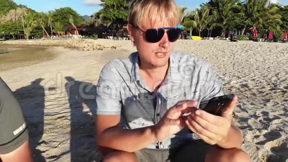 一架无人机和戴墨镜的人用手机管理无人机在热带海滩上的鸟瞰图视频的预览图
