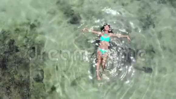 鸟瞰年轻的黑发女人在令人惊叹的清澈大海中游泳在热带岛屿上反射阳光视频的预览图