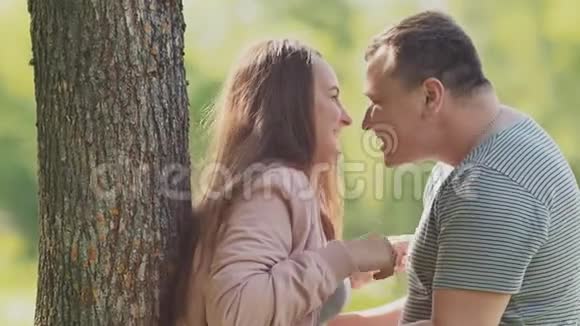一对浪漫的情侣在公园的一棵树旁笑着在拥抱中互相挠痒痒夏天一起快乐视频的预览图