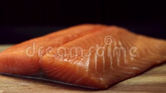 将新鲜美味的三文鱼牛排放在木切割板上隔离在黑色背景上生的红鱼片视频的预览图