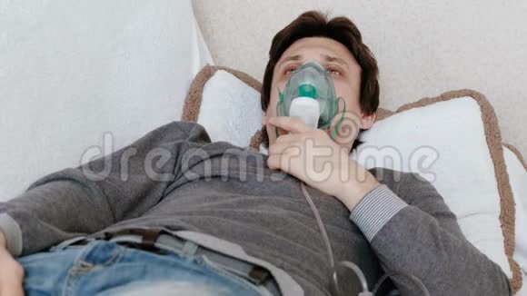 使用雾化器和吸入器进行治疗躺在沙发上的年轻人通过吸入器面罩吸入前景视频的预览图