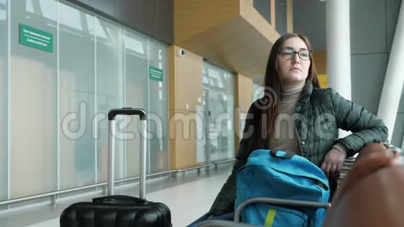 戴眼镜的年轻女子正坐在大厅的机场等待她的航班视频的预览图