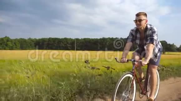 戴墨镜的人骑自行车沿着乡村小径户外年轻的微笑男子骑着老式自行车在农村公路视频的预览图