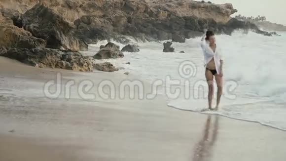 一个穿着白色衬衫的女人沿着海岸散步视频的预览图
