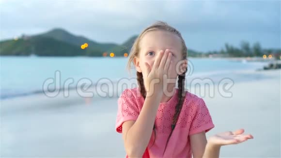 海滩上可爱的小女孩在日落时玩得很开心快乐的孩子看着镜头和亲吻的背景视频的预览图