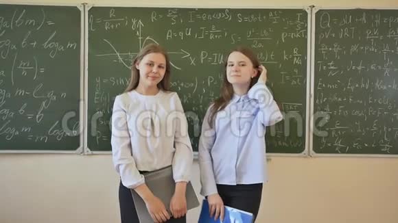 两个女学生在用数学公式画的学校董事会背景下摆姿势视频的预览图
