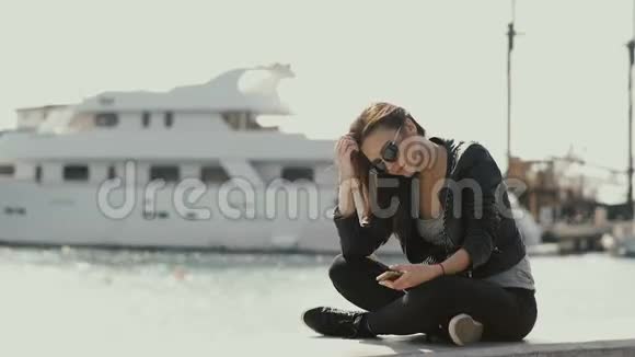 女孩正在用智能手机看着靠近大海的船的背景视频的预览图