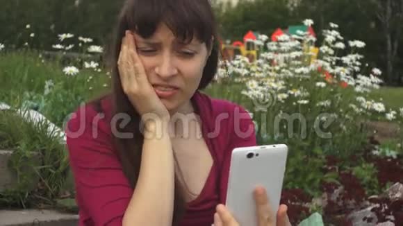 一个牙疼的女人坐在公园的雏菊旁用电话视频的预览图