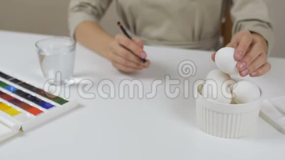 无法辨认的女人在复活节彩蛋上画了一个铅笔素描桌子上有一杯水和一碗鸡蛋视频的预览图
