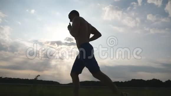 日落时分在乡间小路上慢跑的肌肉男剪影马拉松跑男性慢跑训练概况视频的预览图