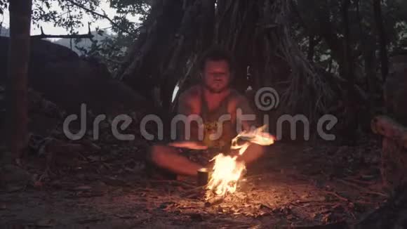 白种人野蛮人在黄昏的热带森林里燃烧小篝火用米饭煮水壶吃晚餐视频的预览图